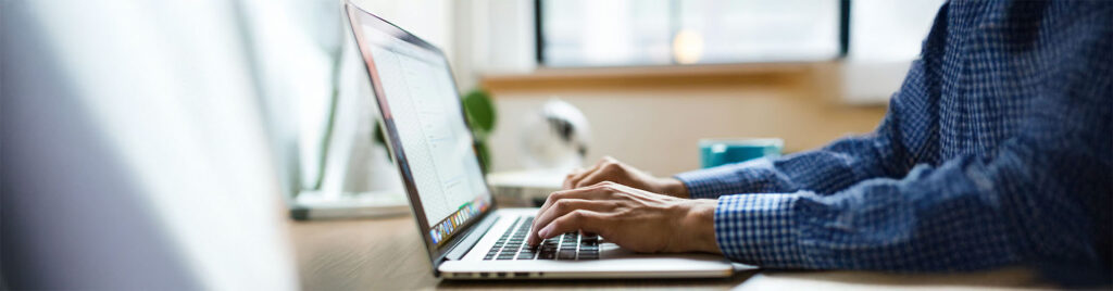 Ein Mann in einem blau weiß karierten Hemd sitzt an einem Laptop